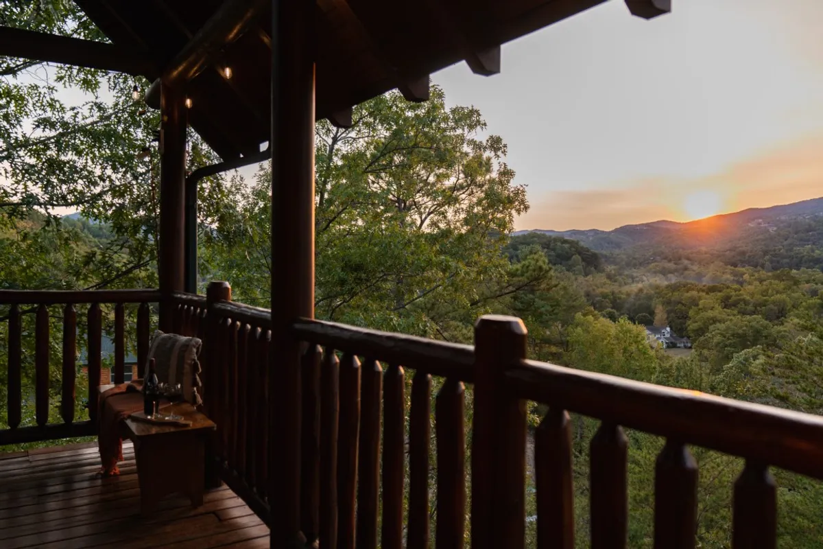 A spacious outdoor deck with a wooden railing offers unobstructed views of the mountains at sunset. A small table is positioned for group gatherings or quiet moments, while the tranquil setting encourages relaxation and conversation. The vibrant colors in the sky create a warm, inviting atmosphere for evening get-togethers.