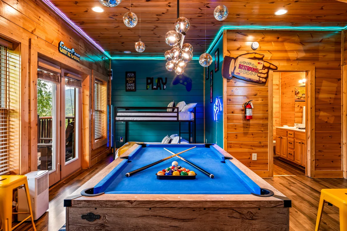 An interior game room with a pool table, disco ball light fixtures, playful wall decor, and bunk beds. The space feels energetic and fun, inviting families to unwind and play together after a day exploring local attractions.