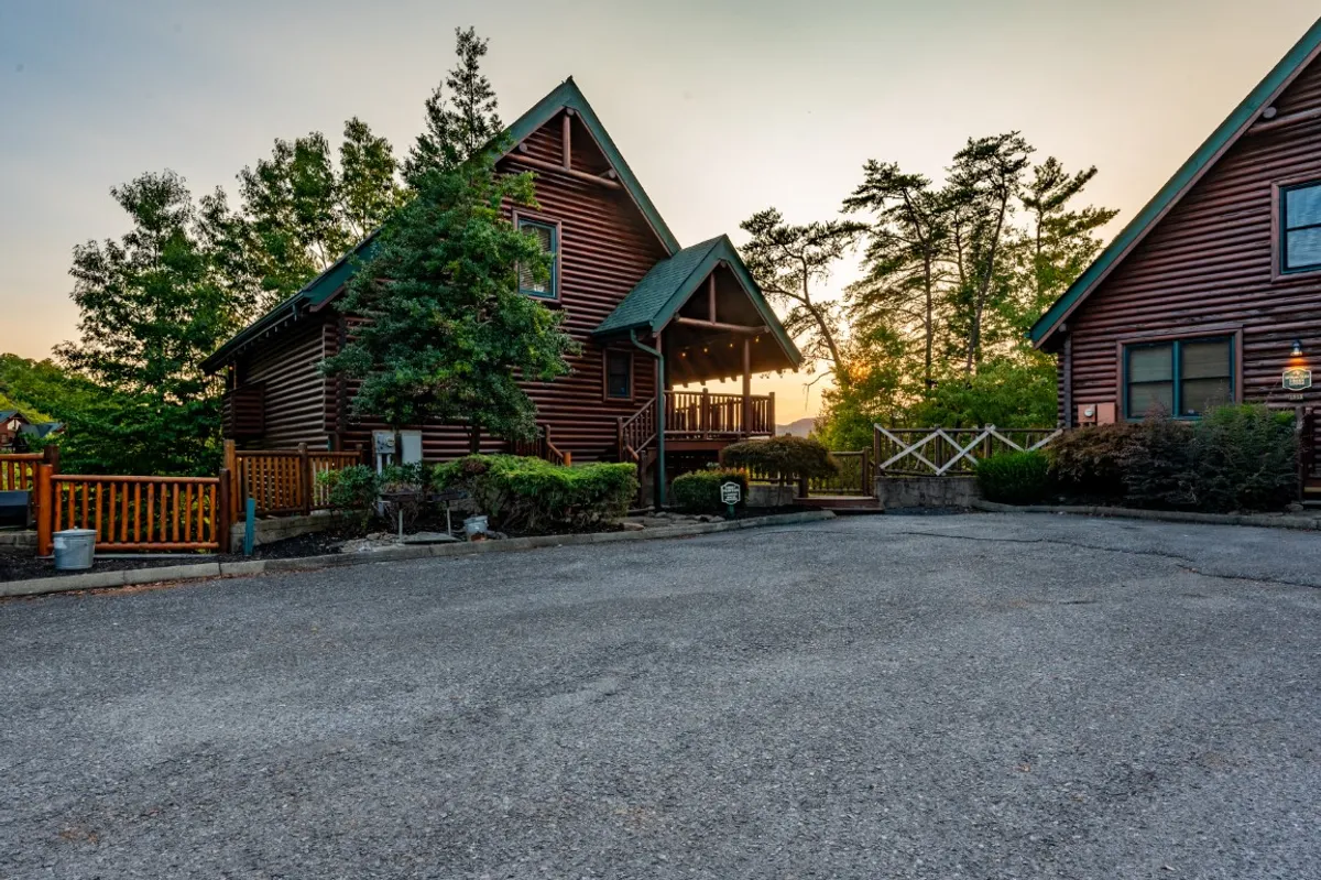 This image captures the log cabin architecture of Smoky Haven Retreat during sunset, with a welcoming front porch and lush green foliage surrounding the home. The soft sunset sky creates a serene and inviting atmosphere, emphasizing the connection to nature and the outdoor adventures that await nearby.