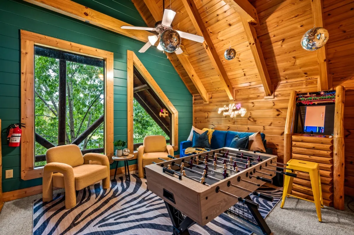 Another entertainment space with a foosball table as the focal point, surrounded by colorful seating and large windows that let in natural light. The room is decorated with playful disco balls and offers views of the outdoors, creating a bright, welcoming, and cheerful environment.
