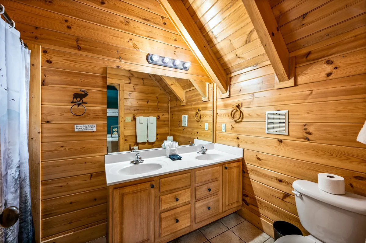 A spa-like bathroom featuring a double sink vanity set against warm wooden walls, a large mirror, and bright lighting. The overall ambiance is cozy and peaceful, evoking the atmosphere of a high-end retreat.