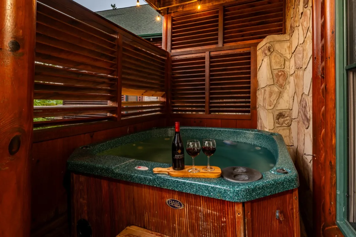 A romantic hot tub scene with a wine bottle, wine glasses, and a wooden serving board set beside the bubbling water. The intimate lighting and view suggest privacy and indulgence, ideal for unwinding after a day of exploration.